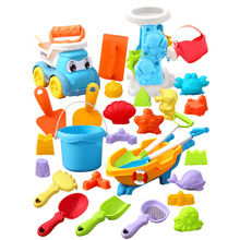 Colorful plastic beach toys including wheelbarrow, bucket, shovel, rake, watering can, molds, and toy truck on white background