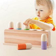 Toddler in orange shirt playing with wooden peg toy featuring pastel-colored rings and simple faces on each peg