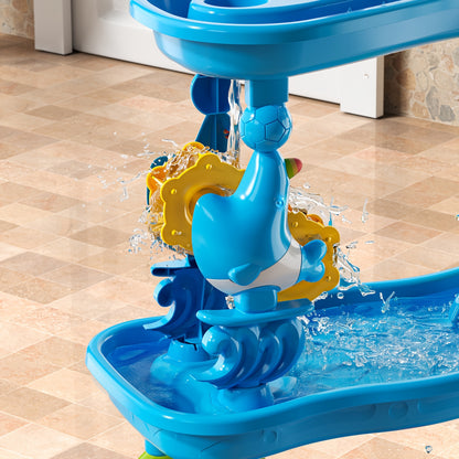 Blue plastic whale-shaped water toy pouring water into a basin with yellow spinning gears on tiled floor