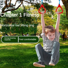 Young boy hanging from red trapeze rings attached to tree branches in a sunny green park setting