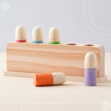 Wooden stacking toy with five peg dolls in pastel red, blue, green, orange, and purple colors on light wooden board