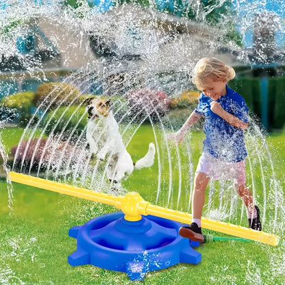 Young child in blue shirt and white shorts playing with a white and brown dog near a rotating water sprinkler on grass