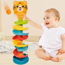 Baby in white outfit playing with colorful spiral ball drop toy with tiger face basket on wooden floor