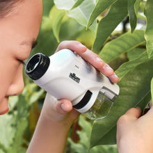 Child examining green leaf closely through a white handheld digital microscope outdoors surrounded by foliage