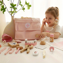Child playing with pink and wooden toy medical kit including stethoscope, thermometer, and medicine bottles on table