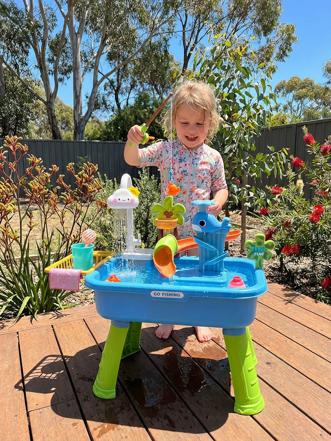 Young child playing with colorful blue and green water fishing activity table outdoors on wooden deck