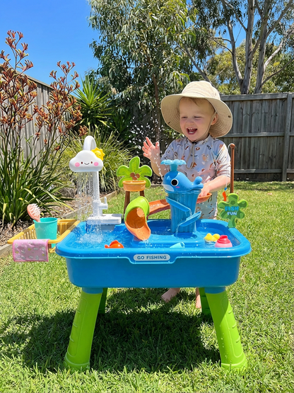 Toddler wearing sun hat playing with water activity table featuring a blue whale and colorful accessories outdoors on grass
