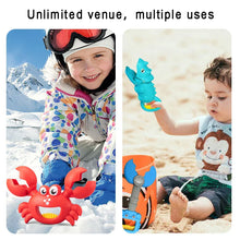 Child playing with red crab toy in snow and toddler holding blue seahorse toy on sandy beach outdoors