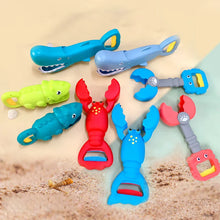 Colorful plastic crab, lobster, crocodile, and clam-shaped beach toys with handles arranged on sand and blue background