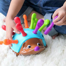 Child playing with colorful plastic hedgehog toy with detachable pegs on soft white surface