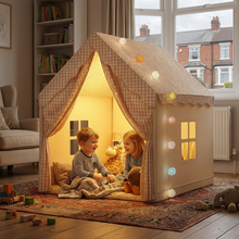 Children playing inside a cozy homemade playhouse with string lights in a home setting.